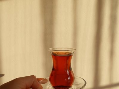 Hands holding a cup of tea near a window.